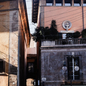 Print of a walkway in Palma, Mallorca, framed by contrasting architectural textures and a vintage street lamp, showcasing Gothic and Art Nouveau styles for home or office decor.