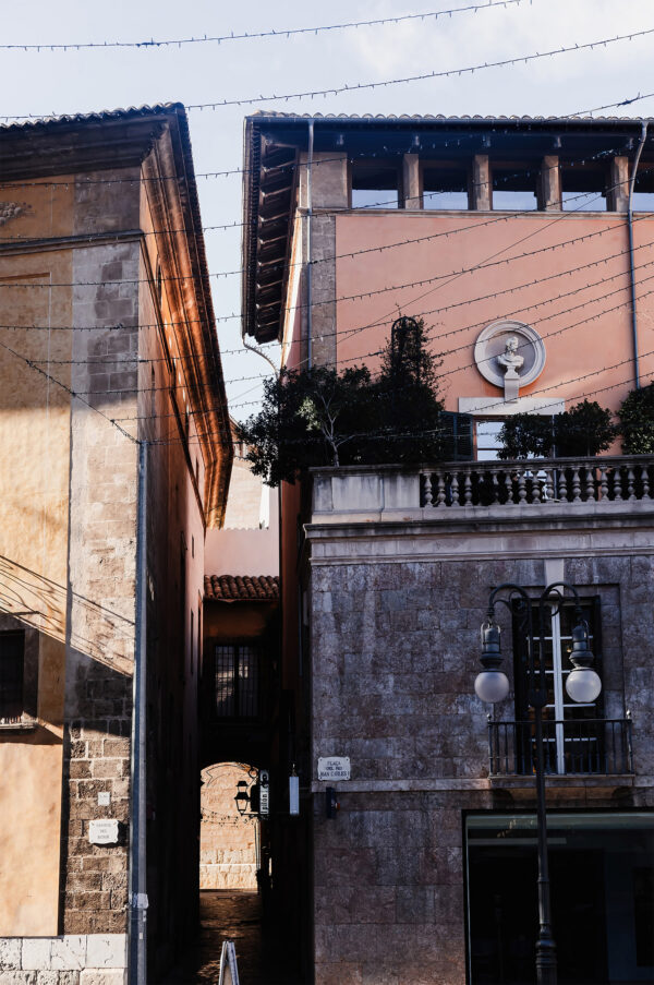 Print of a walkway in Palma, Mallorca, framed by contrasting architectural textures and a vintage street lamp, showcasing Gothic and Art Nouveau styles for home or office decor.