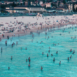 Bondi Beach on a busy summer day, viewed from the north end with the Bondi Pavilion in the background and beachgoers enjoying the ocean.