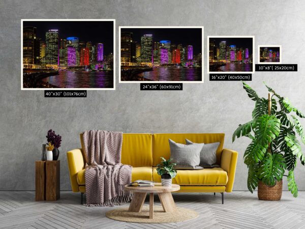 A fine art photograph of Sydney's CBD skyline during Vivid Sydney, taken from Opera Quays. Skyscrapers glow in vibrant purple and red lights, with vivid reflections shimmering across the harbour at night. The image captures the city’s illuminated architecture from a unique perspective, blending light, water, and urban energy.