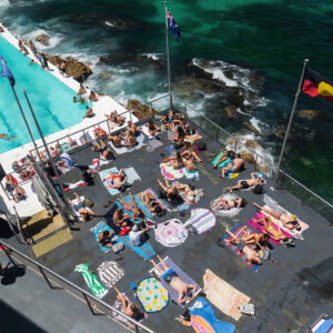 Locals and tourists sunbathing on rooftop deck above Bondi Icebergs, with colourful towels showcasing Sydney’s vibrant beachside lifestyle