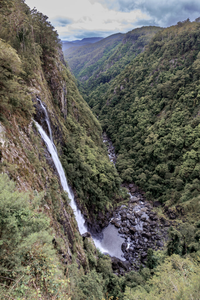 Ellenborough Falls waterfall near Port Macquarie NSW Australia, vertical fine art landscape photograph featuring dramatic cliff drop, misty valley and layered hinterland scenery.