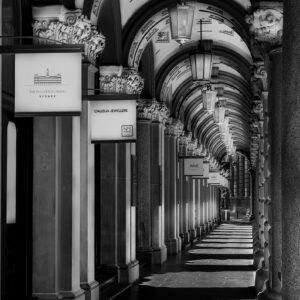 Black and white photograph of The Colonnades outside Fullerton Hotel Sydney showing elegant heritage arches, ornate columns, and dramatic shadow patterns along the walkway.
