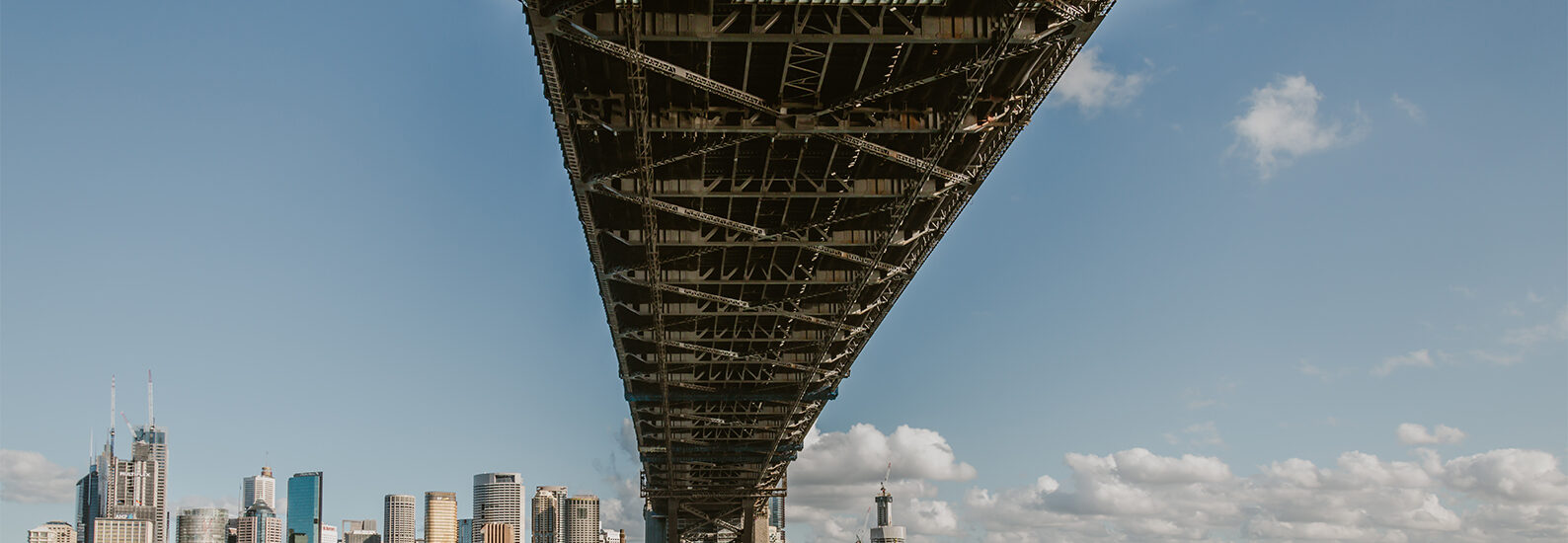 Sydney Harbour Bridge viewed from North Sydney, looking beneath the steel structure towards the Sydney CBD skyline across the harbour.