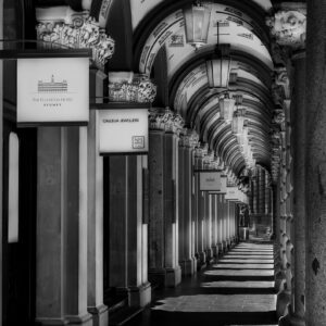 Black and white architectural photograph of The Colonnades in Martin Place, Sydney, featuring ornate sandstone columns, repeating arches, hanging lanterns and dramatic sunlight casting geometric shadows along the historic walkway.
